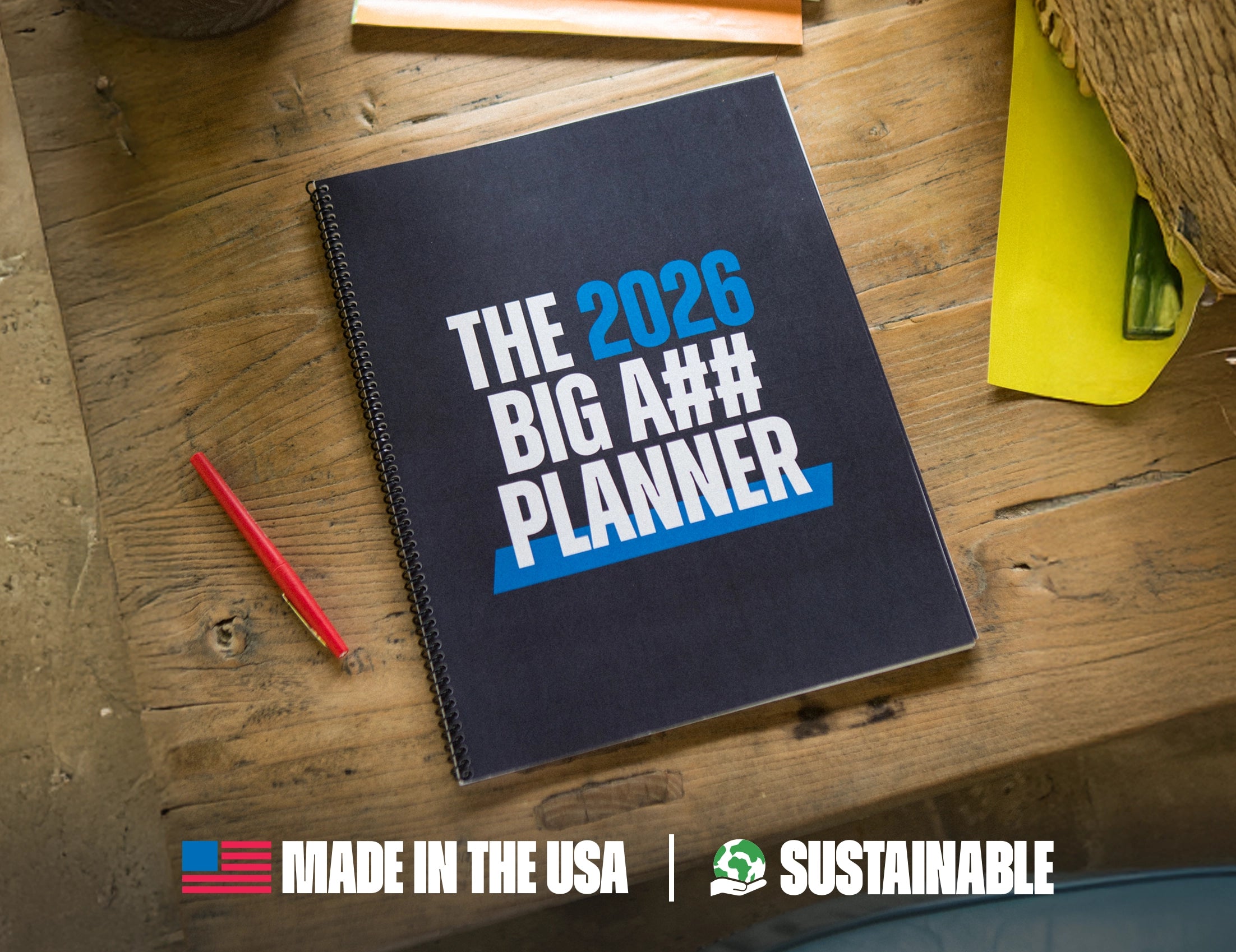 Planner with text 'The 2026 Big A$$ Planner' on a wooden surface, with a red pen and yellow item.