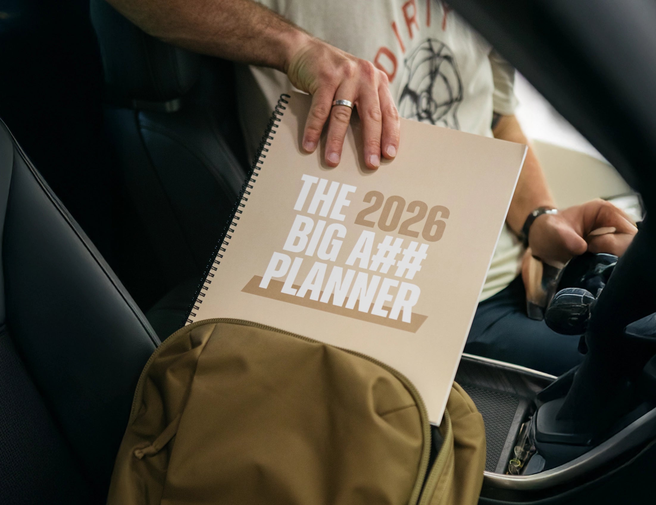 Person holding a planner titled 'The 2026 Big A$$ Planner' in a car.