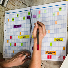 Person using a spiral-bound planner with colorful stickers on a wooden surface