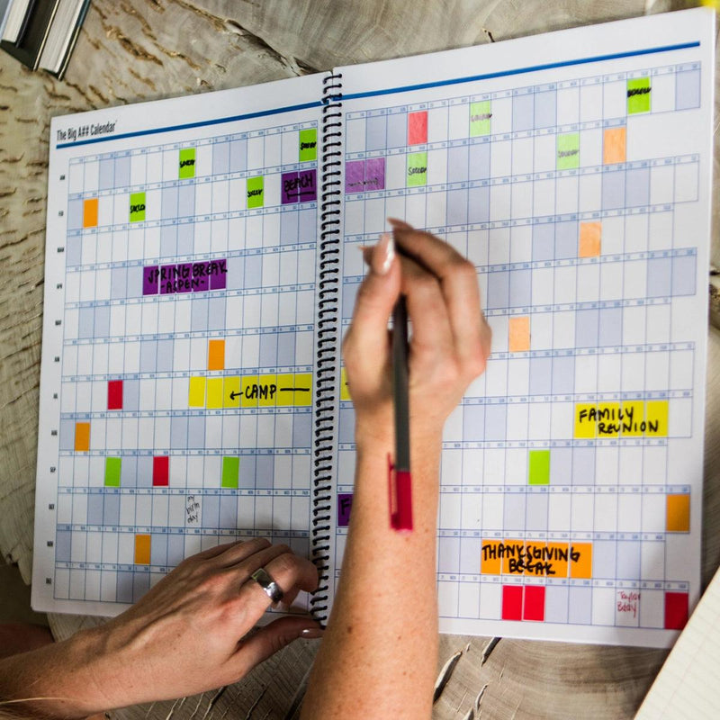 Person using a spiral-bound planner with colorful stickers on a wooden surface